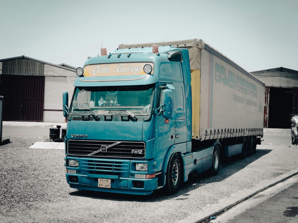 A blue Volvo truck parked outside a warehouse in an industrial area, daytime scene.